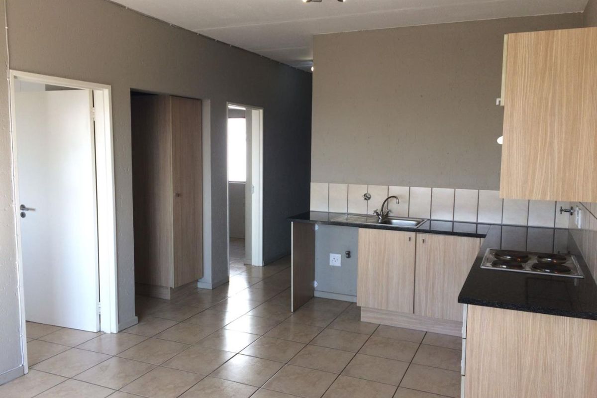 A functional kitchen area featuring built-in cabinetry, laminate countertops, a stainless steel sink, and an integrated electric hob with tiled flooring throughout.
