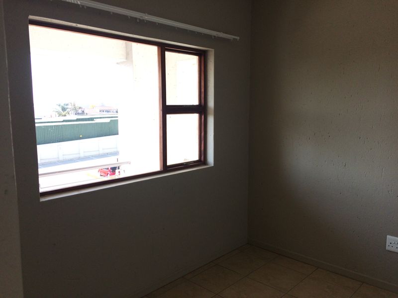 An empty bedroom featuring tiled flooring and a timber-framed window with views of the surrounding area.