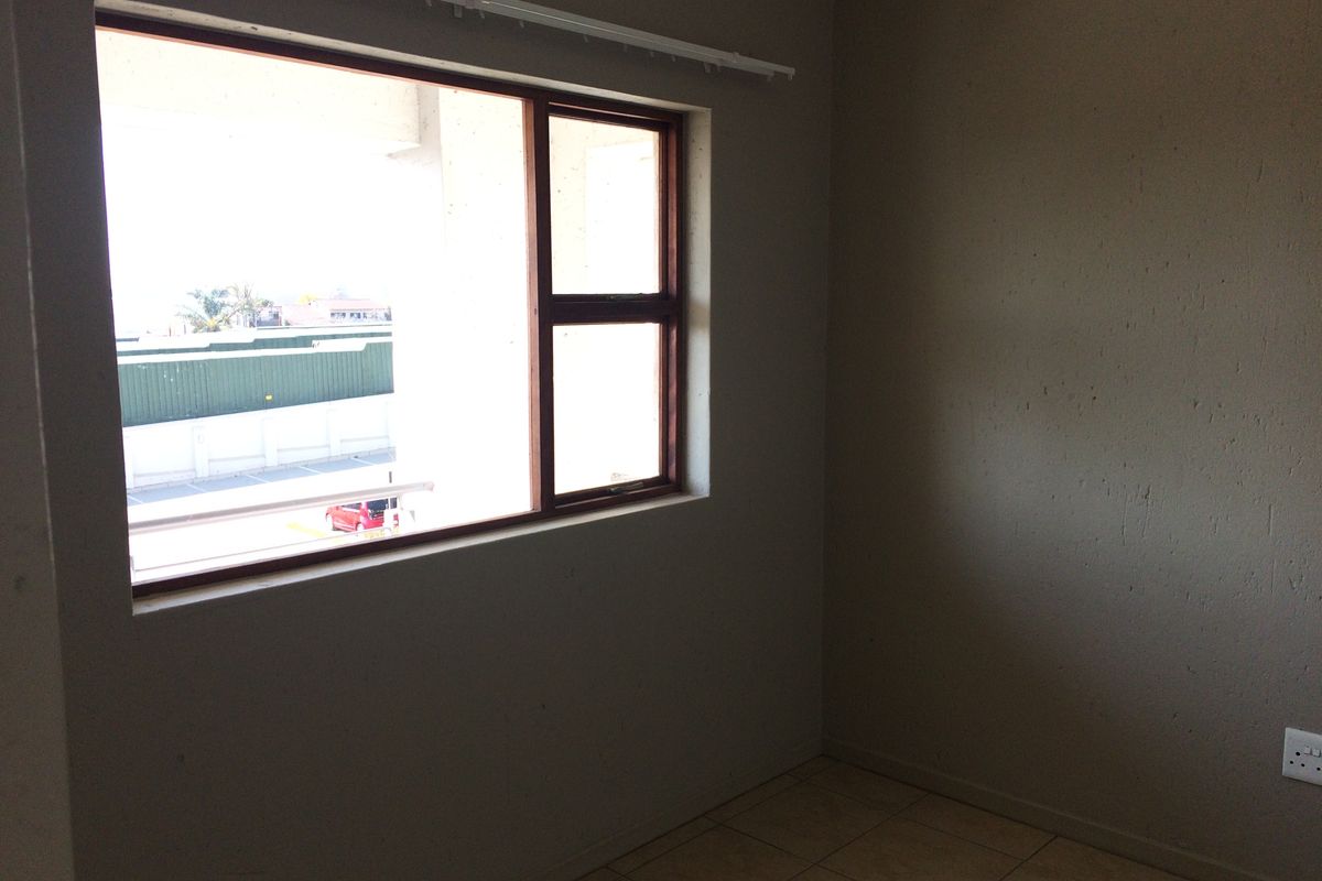 An empty bedroom featuring tiled flooring and a timber-framed window with views of the surrounding area.