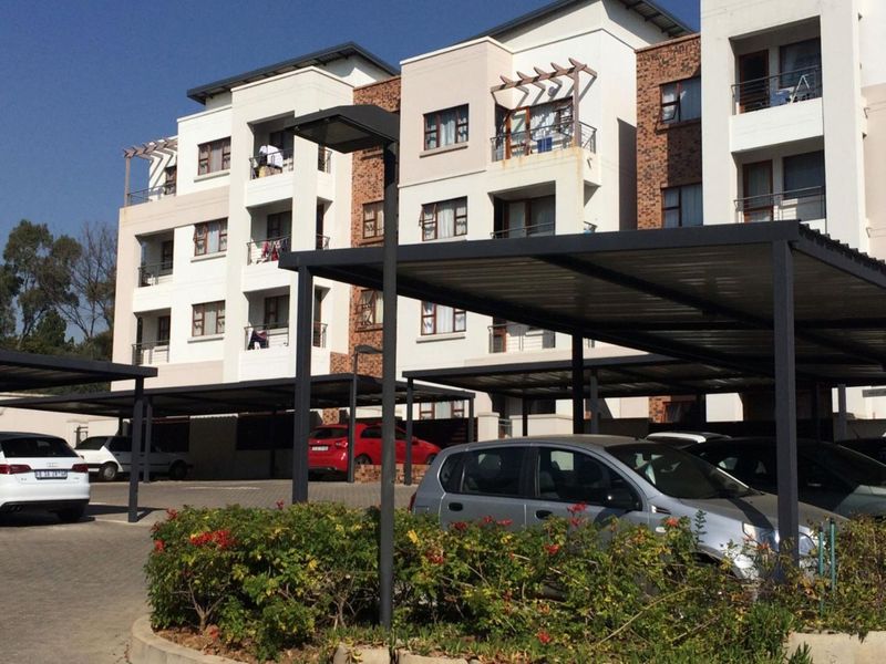 Exterior view of a modern apartment complex featuring multi-story residential units with balconies and dedicated covered parking bays.