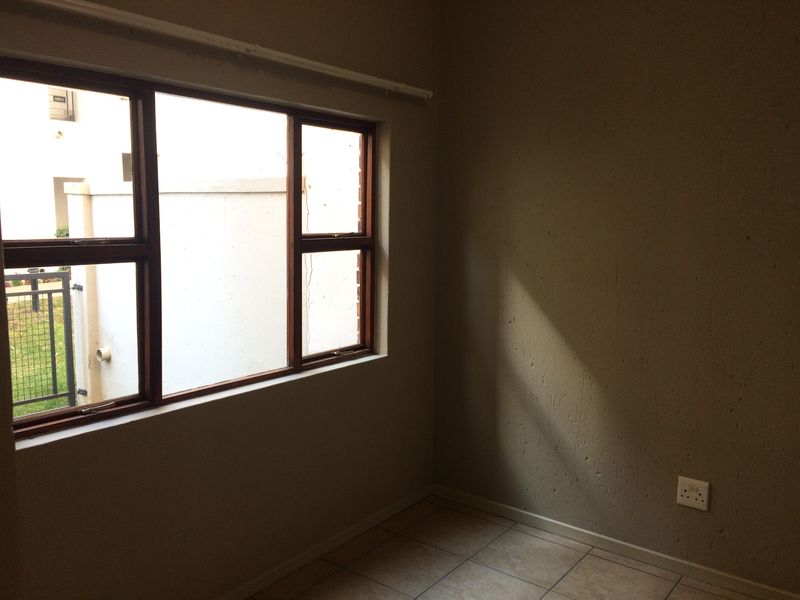 An empty bedroom featuring tiled flooring, timber-framed windows, and a neutral wall finish, offering a blank canvas for potential interior design updates.