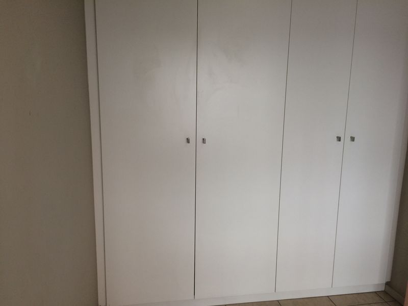 A bedroom featuring white built-in cupboards with simple hardware, providing ample storage space.