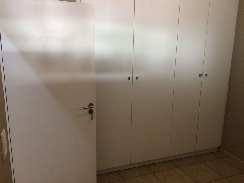 A clean bedroom interior featuring neutral tiled flooring and ample built-in cupboard storage with a modern white finish.