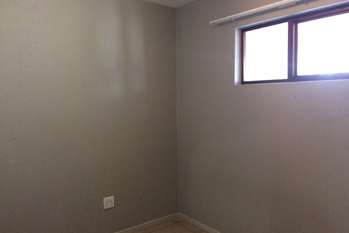 An empty bedroom featuring tiled flooring, a window with a curtain track, and neutral wall finishes.