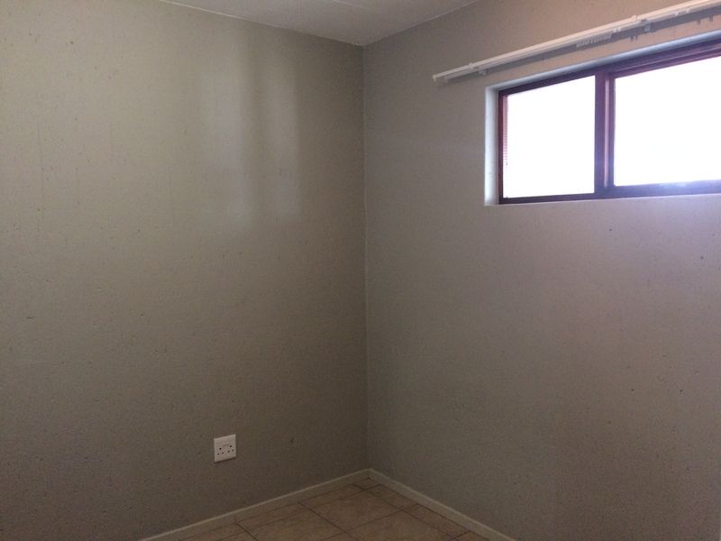 An empty bedroom featuring tiled flooring, a window with a curtain track, and neutral wall finishes.