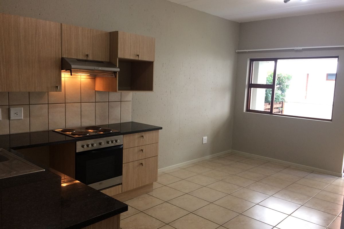 A clean, empty kitchen featuring light wood cabinetry, dark granite countertops, an integrated oven and hob, and neutral tiled flooring.