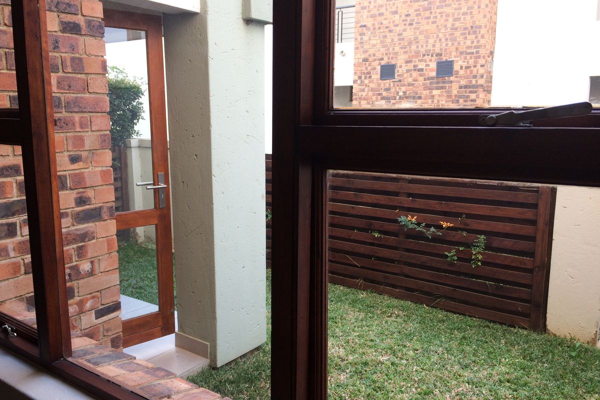 A view from inside looking out onto a private rear garden area featuring a small lawn, timber fencing, and a wooden door.