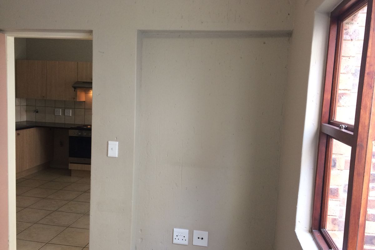 An empty living area featuring tiled floors and a timber window, with a view into the adjacent kitchen space.