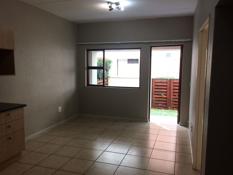 An open-plan living and kitchen area featuring tiled flooring, neutral wall tones, and direct access to an outdoor space through a glass door.
