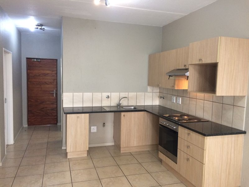 A functional kitchen featuring light wood cabinetry, dark countertops, built-in oven and hob, and tiled flooring, leading to a separate entrance area.