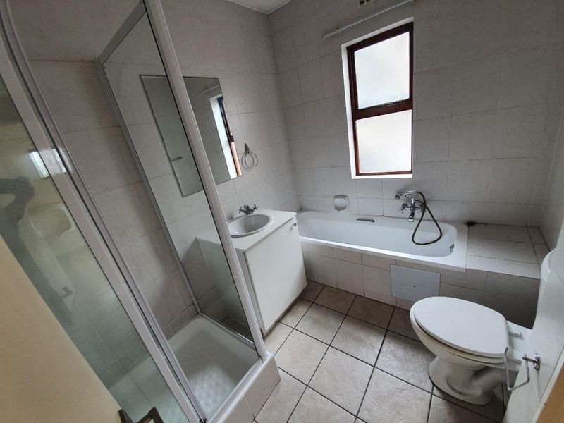A functional bathroom featuring a separate shower enclosure, bathtub, vanity basin, and toilet with neutral wall and floor tiling.