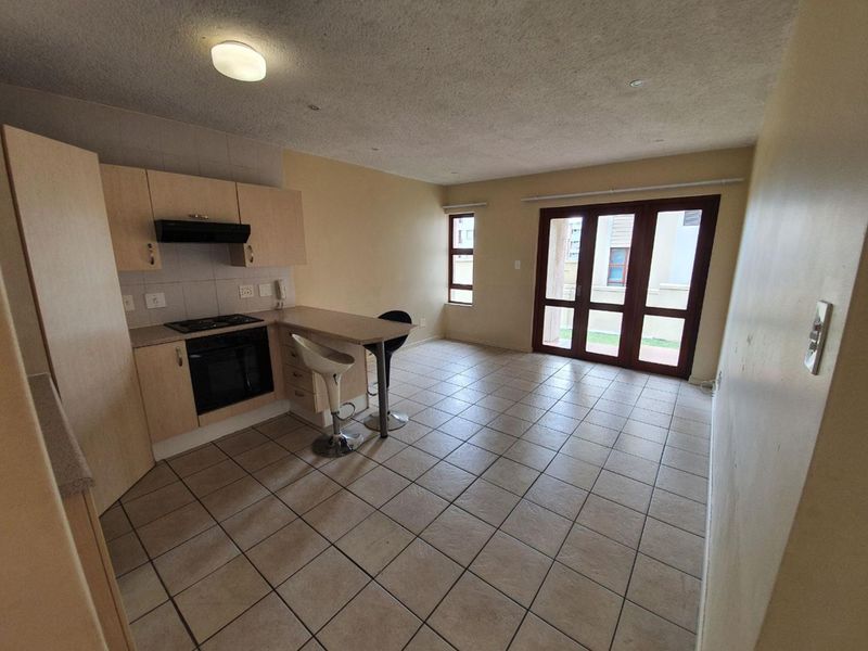 Open-plan kitchen and living area featuring tiled flooring, built-in cabinetry with integrated appliances, and large glass doors leading to the exterior.