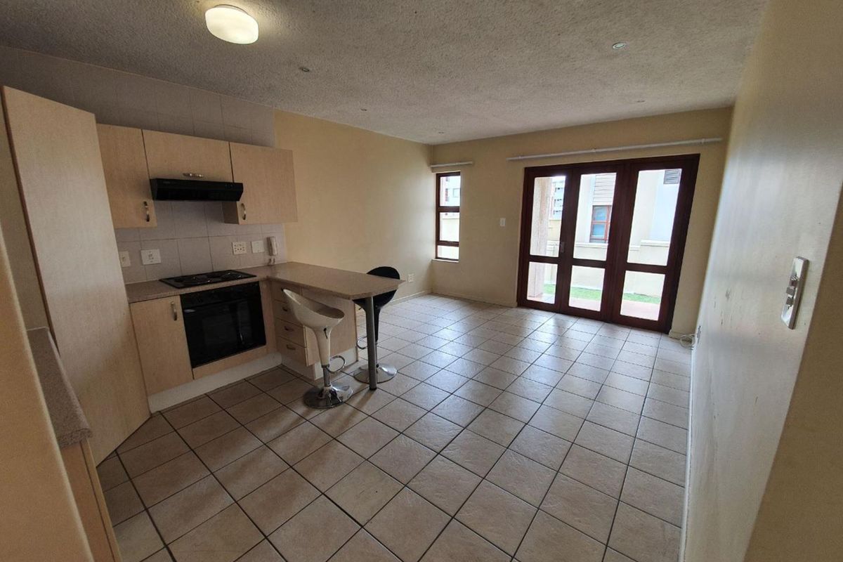Open-plan kitchen and living area featuring tiled flooring, built-in cabinetry with integrated appliances, and large glass doors leading to the exterior.