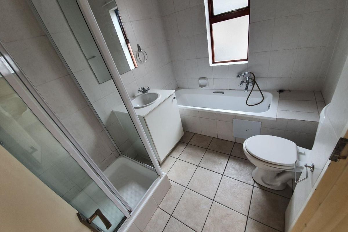A functional bathroom featuring a shower enclosure, bathtub, vanity with washbasin, and toilet, finished with neutral wall and floor tiling.