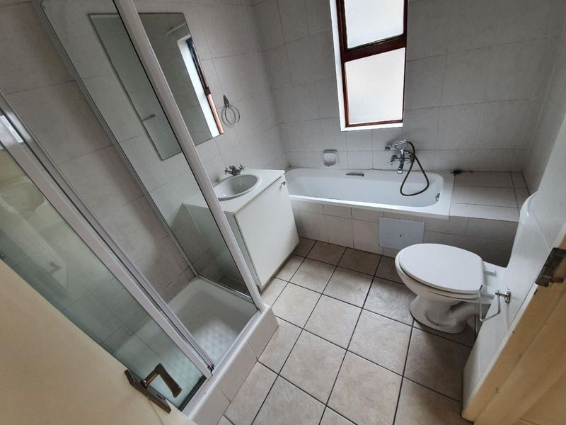 A functional bathroom featuring a shower enclosure, bathtub, vanity with washbasin, and toilet, finished with neutral wall and floor tiling.