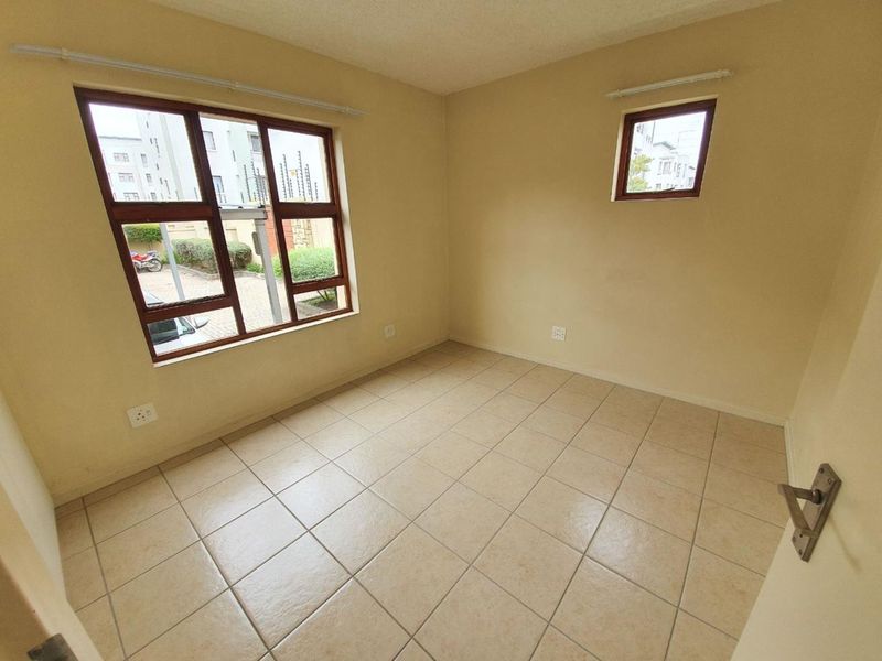 A vacant bedroom featuring neutral tiled flooring and natural light from multiple windows, offering a blank canvas for personalization.