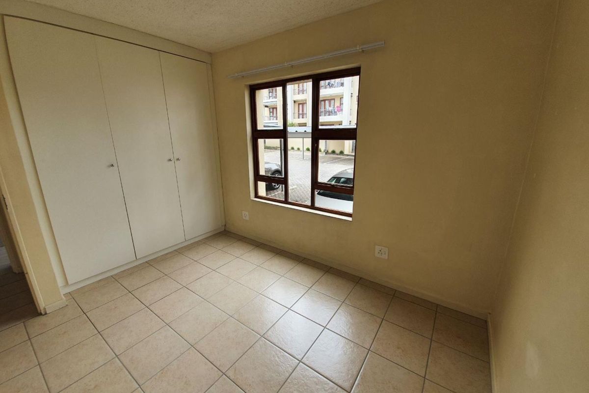 An empty bedroom featuring tiled flooring, built-in cupboards, and a window overlooking the complex parking area.