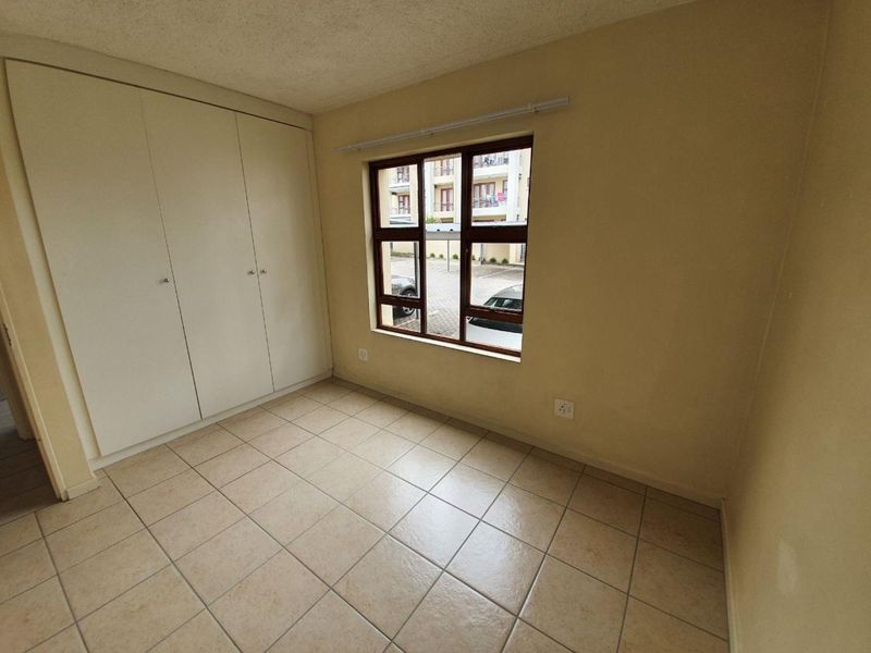An empty bedroom featuring tiled flooring, built-in cupboards, and a window overlooking the complex parking area.