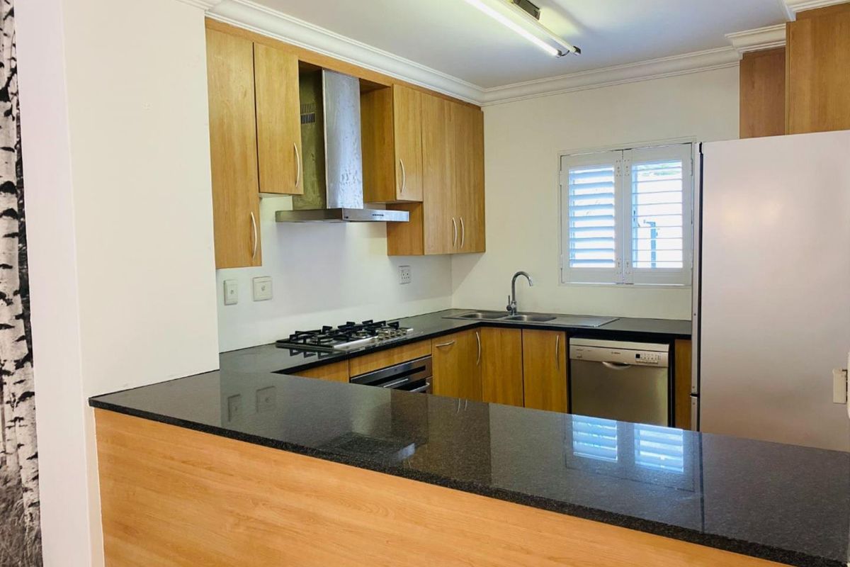 A functional kitchen featuring wooden cabinetry, granite countertops, a gas hob, built-in oven, and plantation shutters, offering a clean and practical workspace.