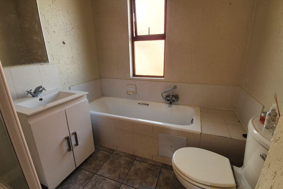 A functional bathroom featuring a built-in vanity, bathtub, and shower enclosure, requiring cosmetic updates to improve the overall aesthetic and finish.
