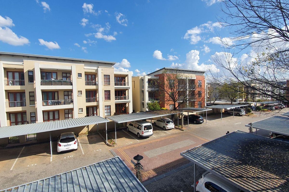 An elevated view of the apartment complex exterior, featuring paved parking areas with covered carports and multi-story residential building facades.