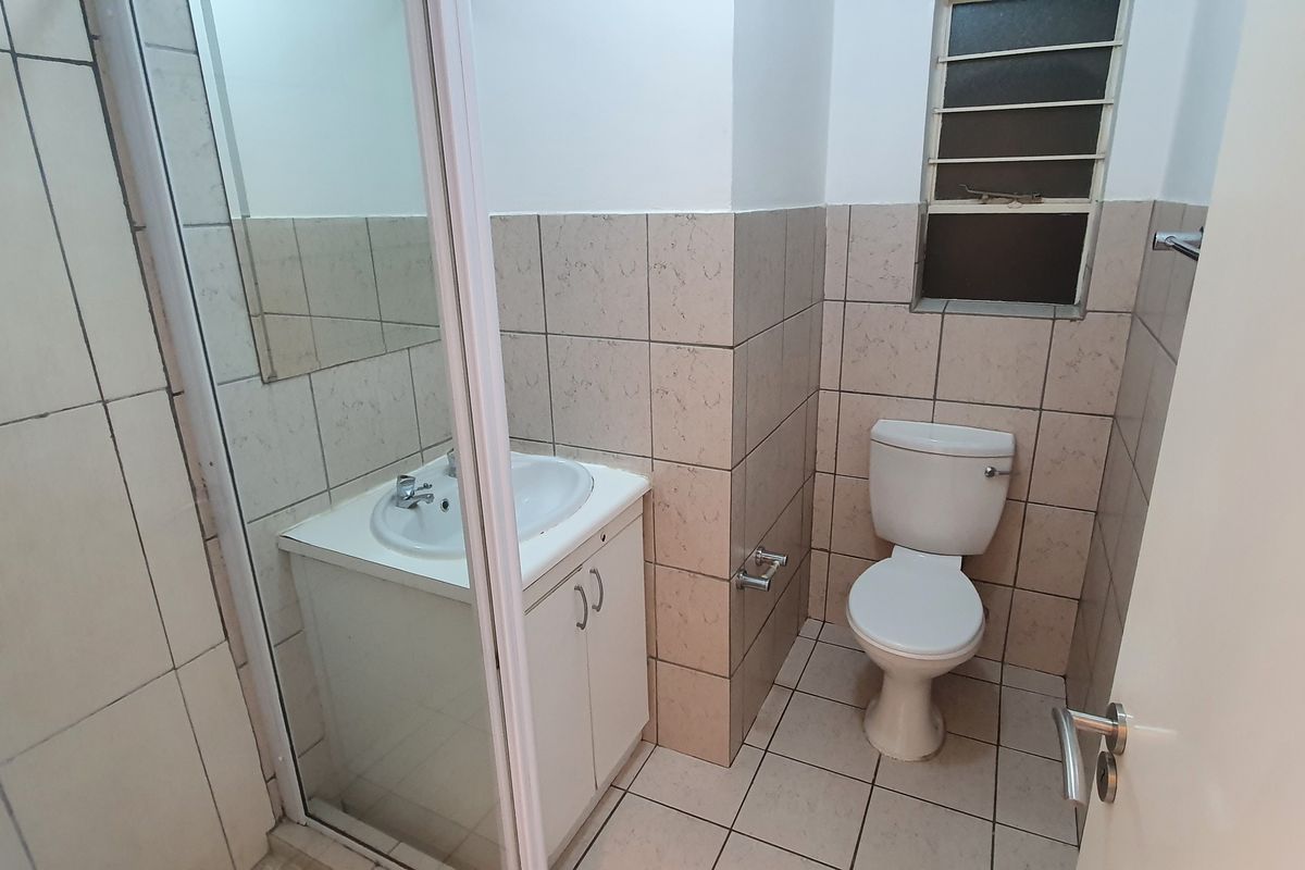 A functional bathroom featuring a shower enclosure, a vanity basin with storage, and a standard toilet, finished with neutral wall and floor tiling.