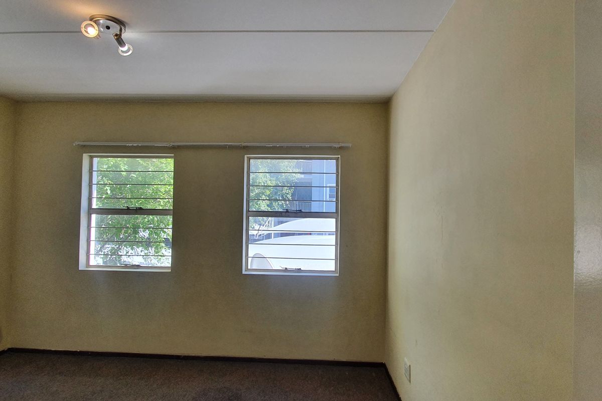 An empty bedroom featuring dual windows with security bars, neutral wall finishes, and carpeted flooring.