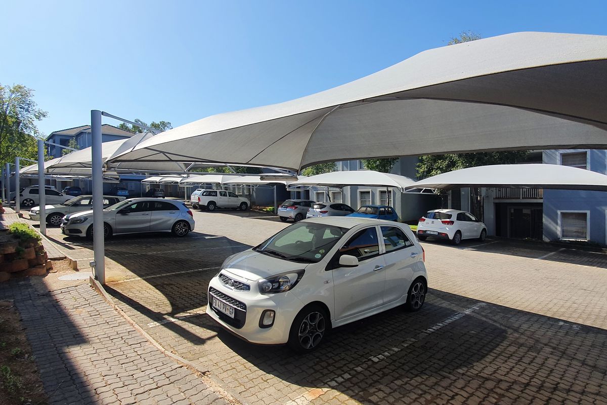Outdoor parking area featuring multiple covered shade-cloth carports situated within the apartment complex grounds.