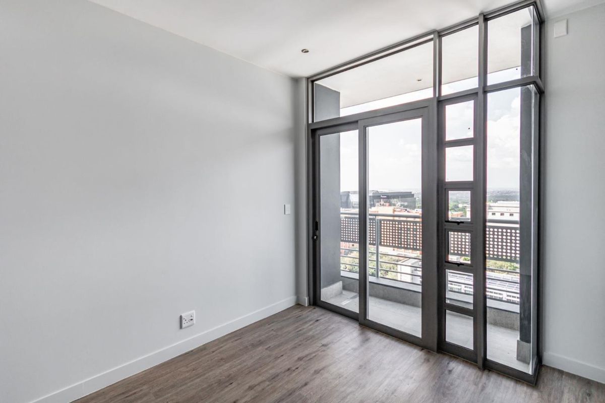 A bright, empty bedroom featuring modern laminate flooring, recessed lighting, and large sliding glass doors leading to a private balcony.