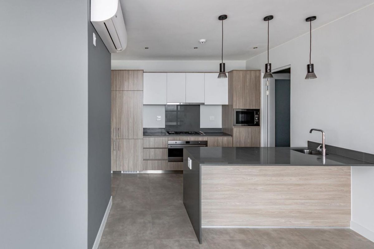 Modern kitchen featuring sleek wood-tone and white cabinetry, stone countertops, integrated appliances, and a functional island with a sink, finished with contemporary pendant lighting.