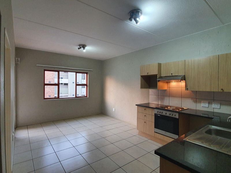 Open-plan living area featuring a functional kitchen with built-in cabinetry, electric stove, oven, and tiled flooring throughout.