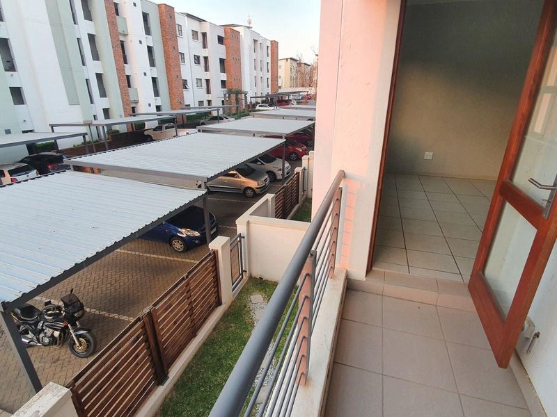 A private balcony overlooking the apartment complex parking area, featuring tiled flooring and a metal balustrade with direct access to the interior.
