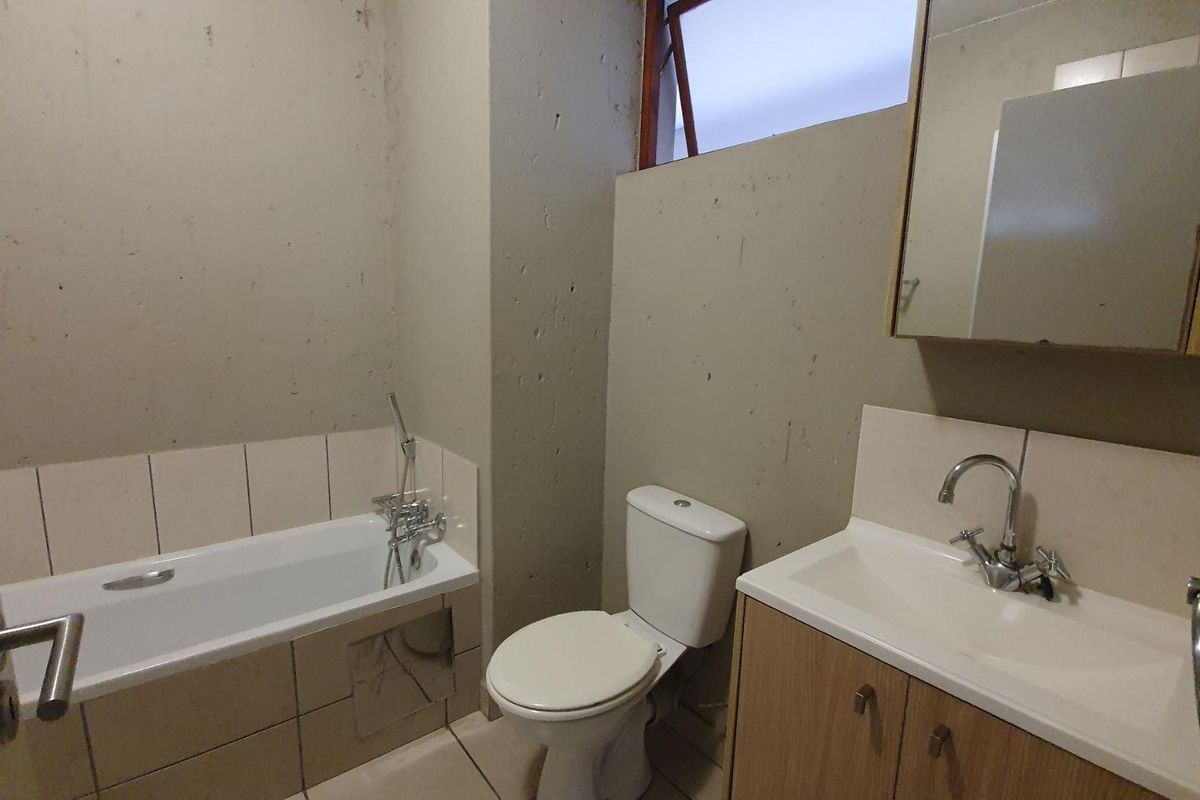 A functional bathroom featuring a bathtub, toilet, and vanity cabinet with a washbasin, requiring cosmetic updates to the wall finishes.