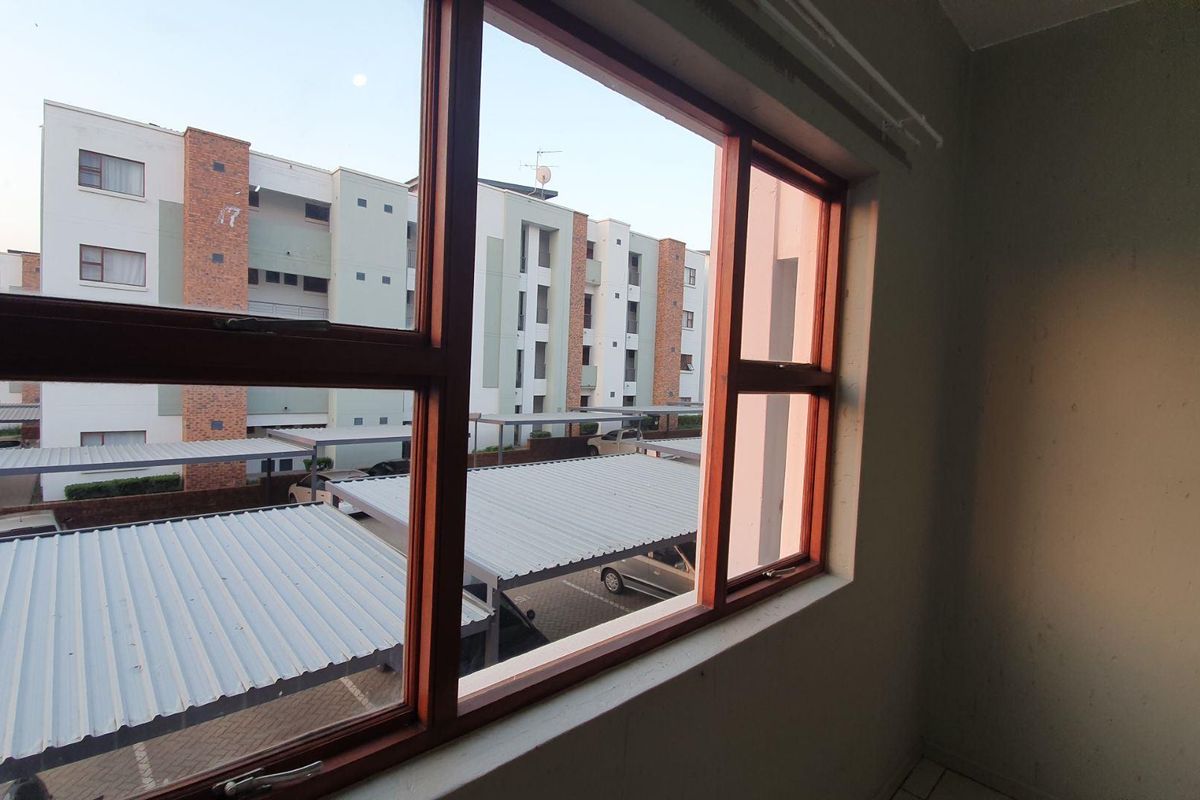 An empty bedroom interior featuring a large timber-framed window with views over the apartment complex parking area.