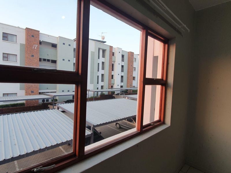 An empty bedroom interior featuring a large timber-framed window with views over the apartment complex parking area.