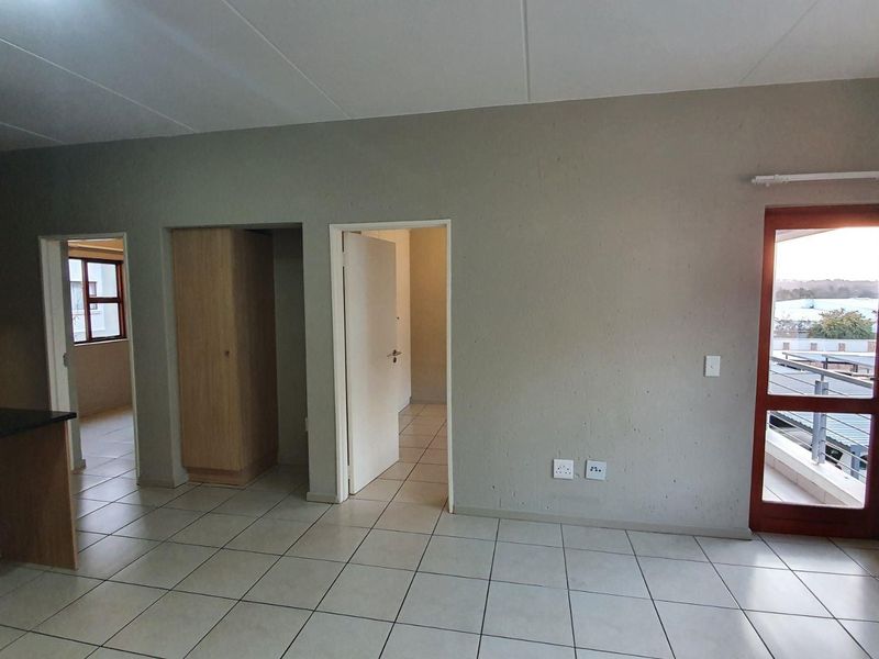 An open-plan living area featuring tiled flooring, built-in kitchen cabinetry with granite countertops, and direct access to an outdoor balcony.