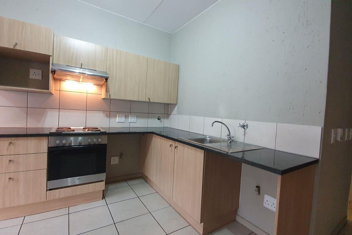 A functional kitchen featuring light wood-finish cabinetry, granite countertops, a built-in oven and hob, and tiled flooring.