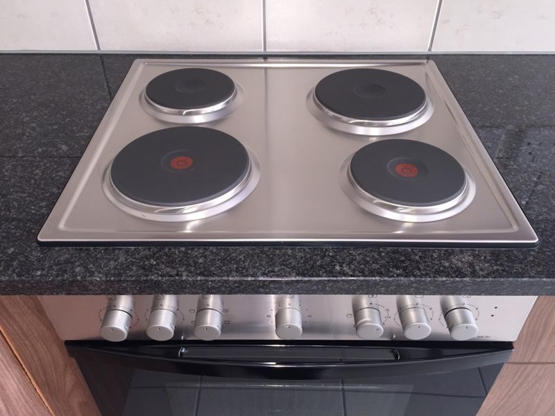A clean, well-maintained stainless steel electric hob and built-in oven set into a dark granite countertop with a tiled splashback.
