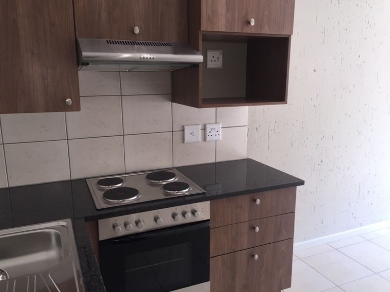 A clean, modern kitchen featuring dark wood cabinetry, granite countertops, a built-in electric oven and hob, and a stainless steel sink.