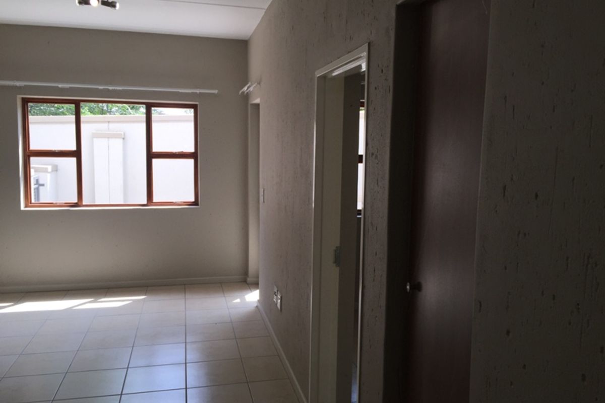 An empty living area featuring neutral tiled flooring, a ceiling-mounted spotlight fixture, and a timber-framed window allowing natural light.