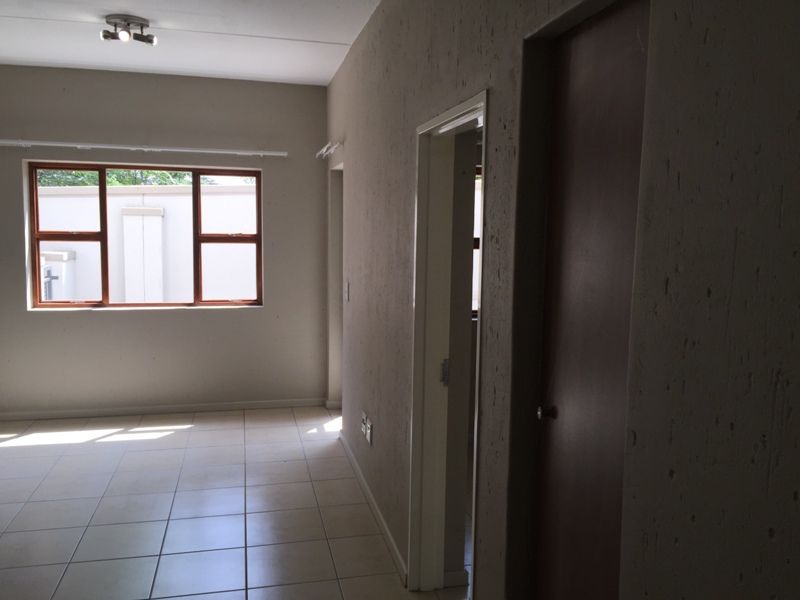 An empty living area featuring neutral tiled flooring, a ceiling-mounted spotlight fixture, and a timber-framed window allowing natural light.