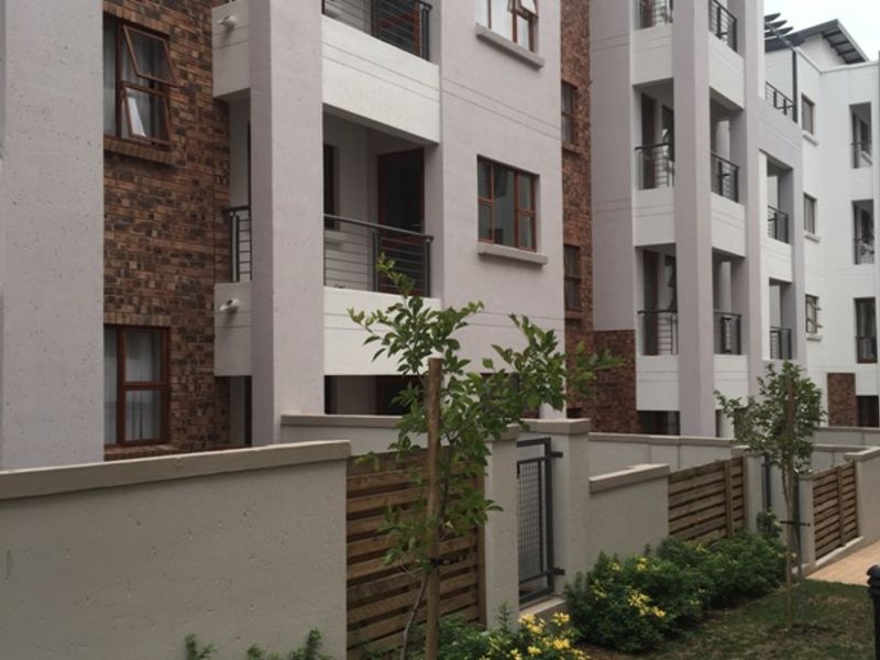 Exterior view of a modern apartment complex featuring brick and plaster finishes, private balconies with metal railings, and a landscaped garden area.