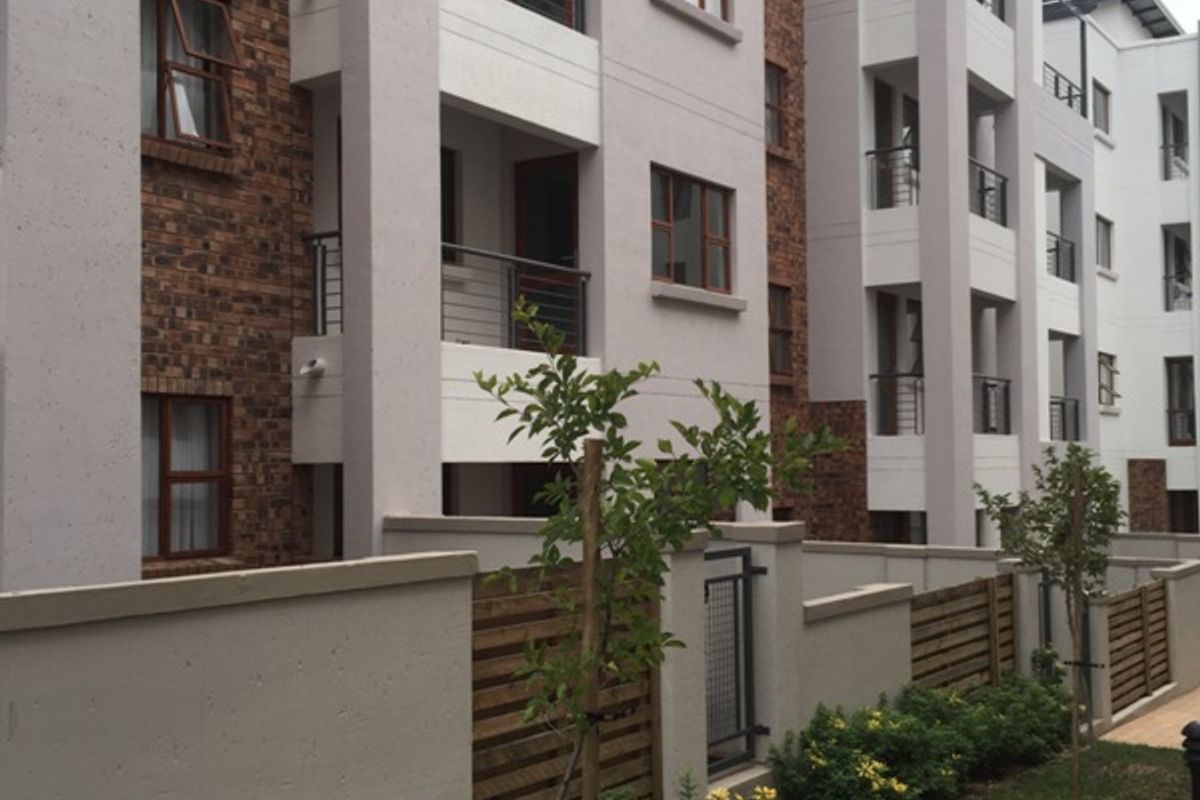Exterior view of a modern apartment complex featuring brick and plaster finishes, private balconies with metal railings, and a landscaped garden area.