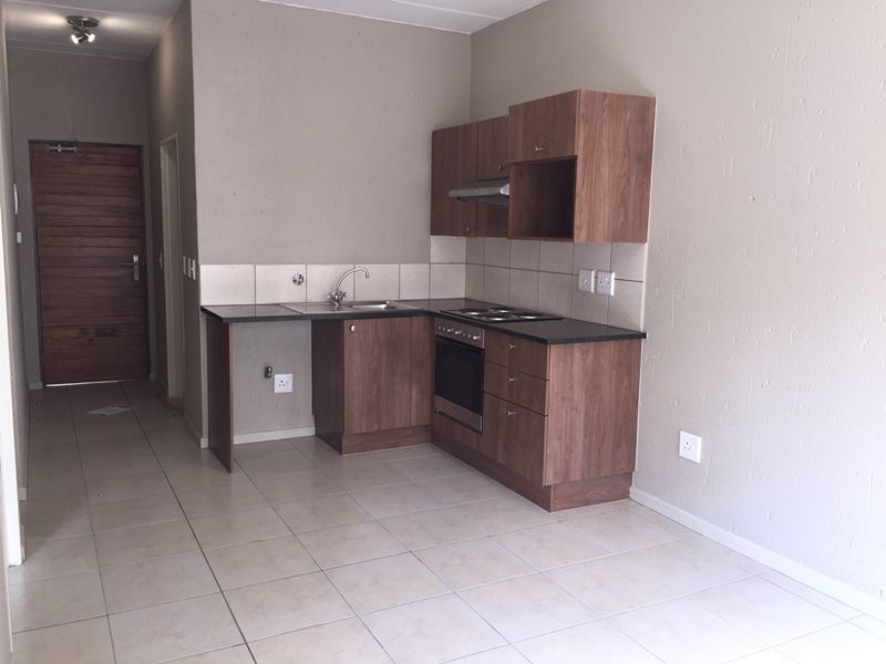 Compact kitchen featuring wood-finish cabinetry, dark countertops, built-in oven, hob, and extractor fan, set against a neutral tiled floor and backsplash.