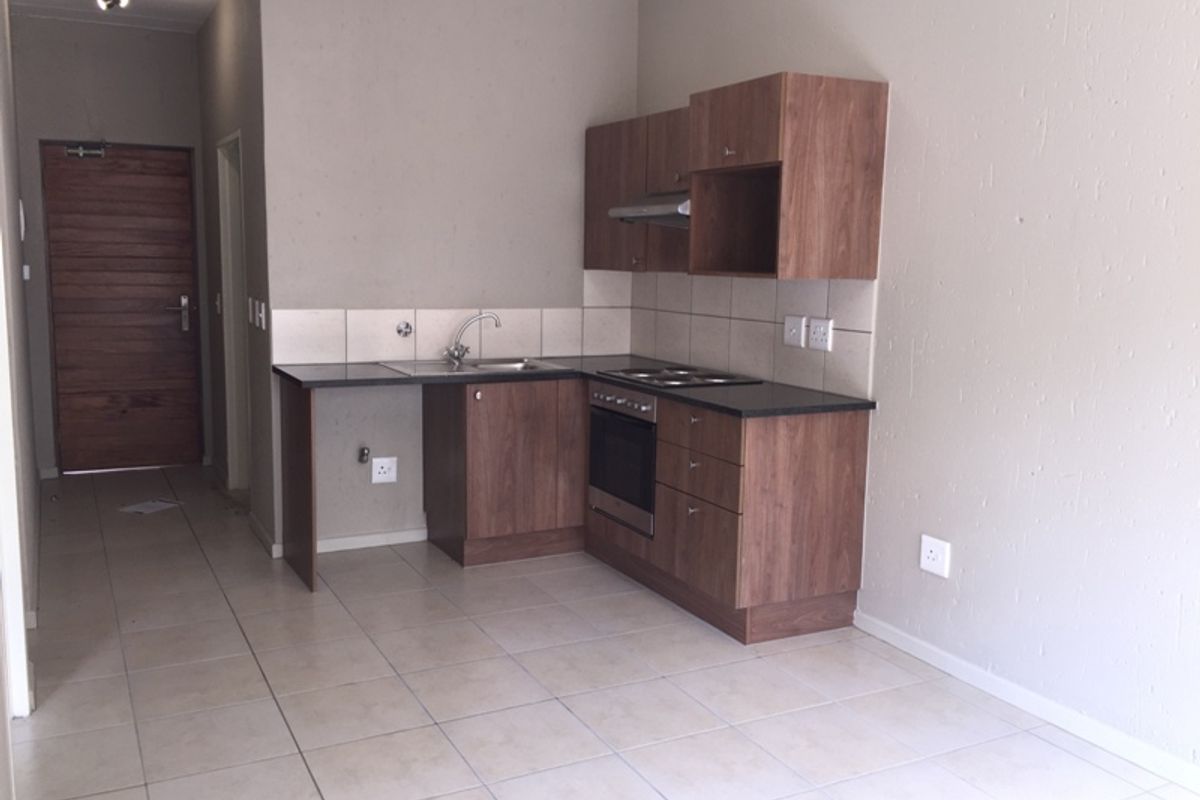 Compact kitchen featuring wood-finish cabinetry, dark countertops, built-in oven, hob, and extractor fan, set against a neutral tiled floor and backsplash.