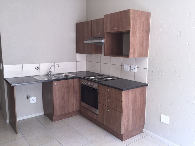 Compact kitchen featuring wood-look laminate cabinetry, granite countertops, built-in oven, electric hob, and tiled splashback in a neutral, open-plan setting.