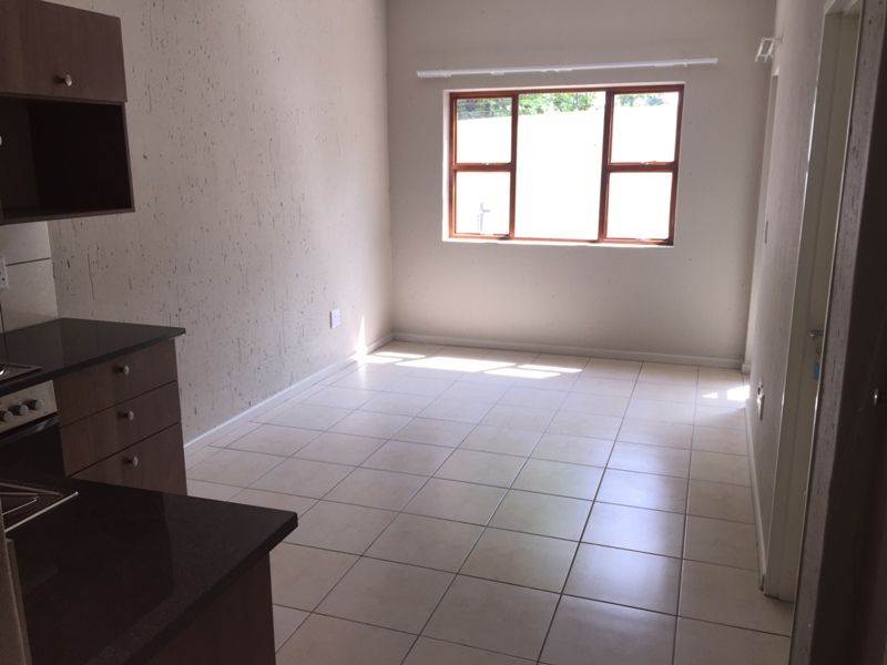 An empty open-plan living and kitchen area featuring tiled flooring, built-in cabinetry with granite countertops, and a window providing natural light.
