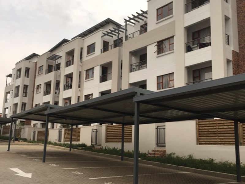 Exterior view of a modern multi-story apartment complex featuring covered parking bays and private balconies for each unit.