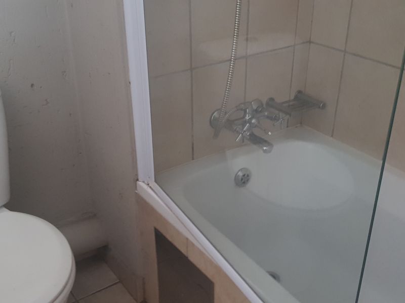 A functional bathroom featuring a standard toilet, a bathtub with a shower mixer, and a glass shower screen with tiled wall surrounds.