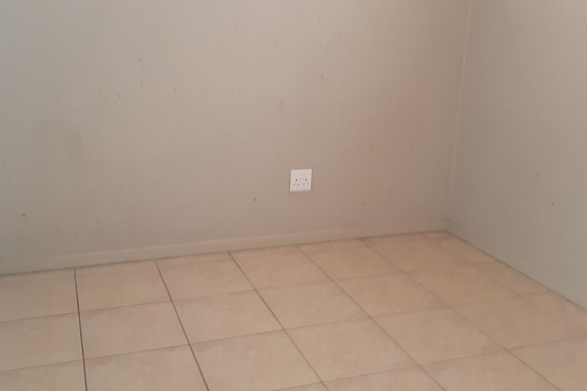 An empty bedroom featuring neutral tiled flooring and plain walls, providing a blank canvas for personalization.